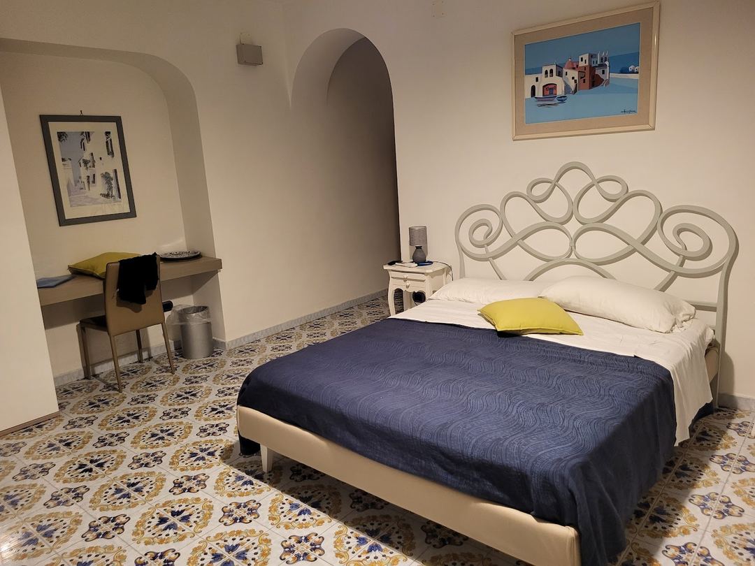 A Mediterranean-style bedroom featuring a white ornate metal bed frame, navy blue bedding, and patterned tile flooring.
